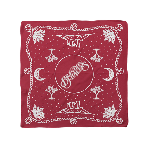 A square red bandana featuring a white desert-themed graphic print with the words 'Brandon Flowers' in a central circle, surrounded by moons, cactus silhouettes, stars, and a rope border.